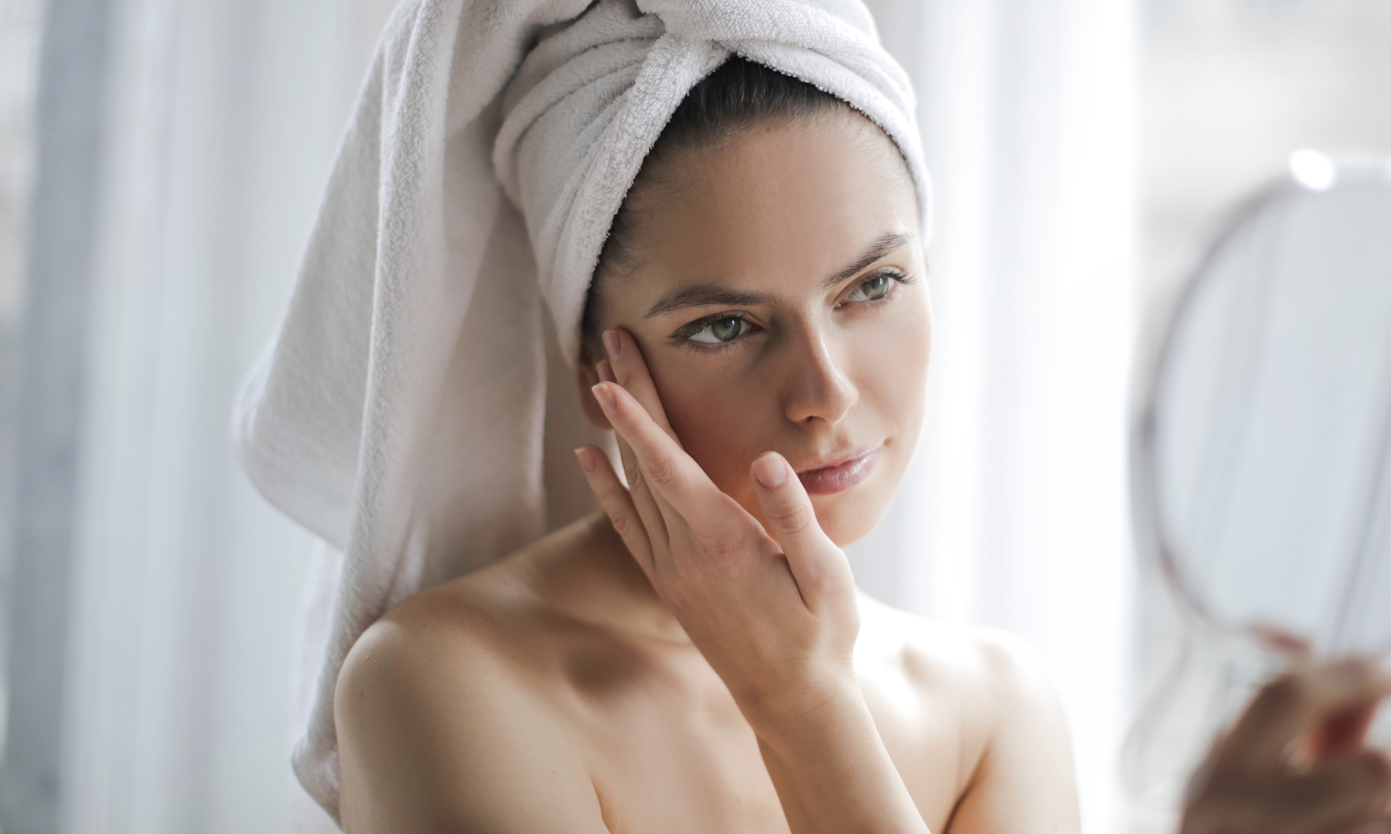 Frau schaut sich mit einem Handspiegel im Gesicht an und fühlt mit ihrer Hand die weiche Haut nach ihrer JetPeel Behandlung in der Beauty Bar Winterhude